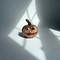 A small carved jack-o'-lantern pumpkin sits on a white surface in sharp window-box style sunlight and shadow.