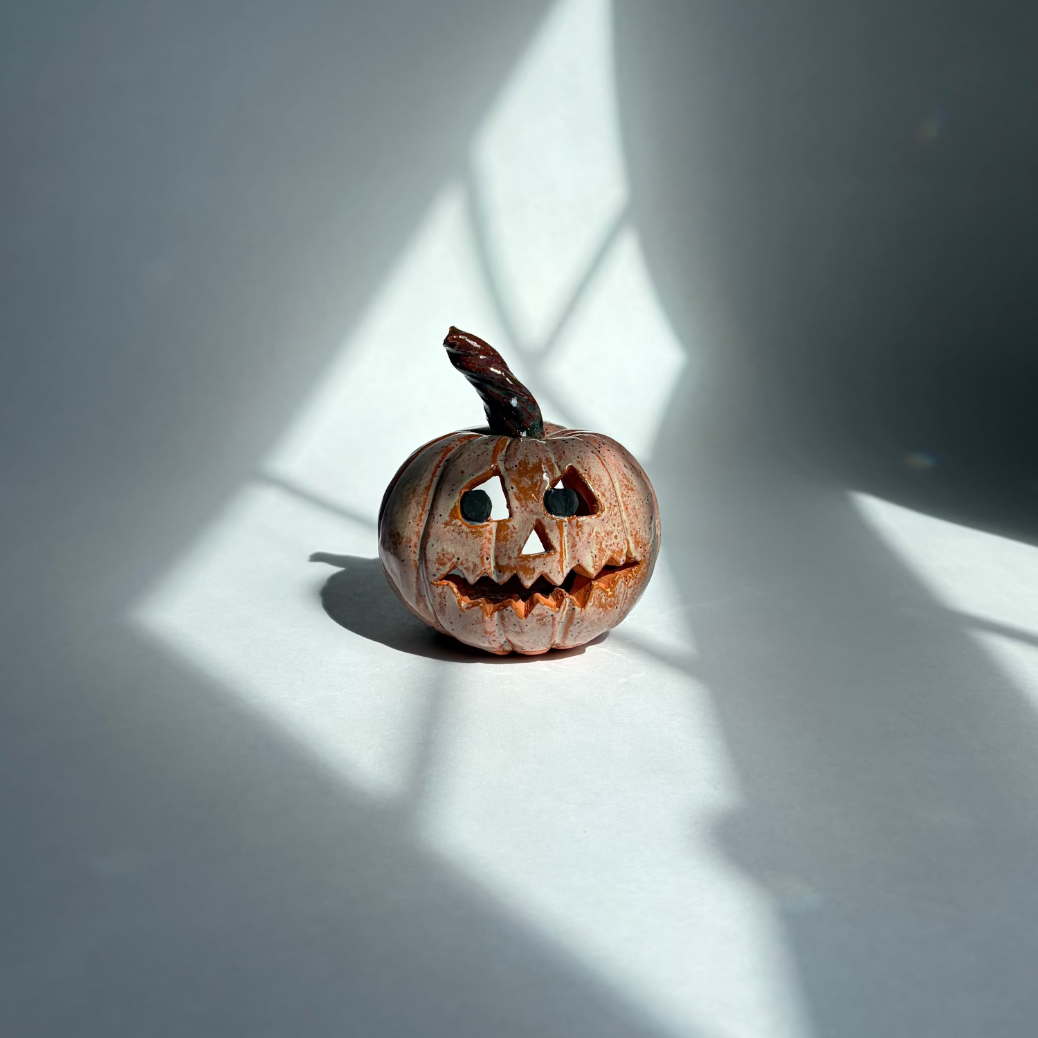 A small carved jack-o'-lantern pumpkin sits on a white surface in sharp window-box style sunlight and shadow.