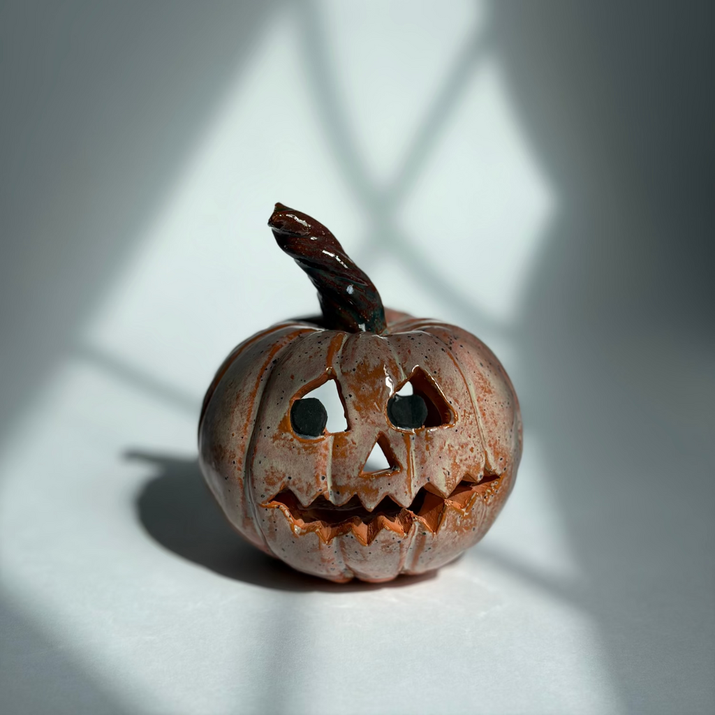 A small carved jack-o'-lantern pumpkin with a dark stem, photographed on a white surface with dramatic window-pane shadows cast across the scene.