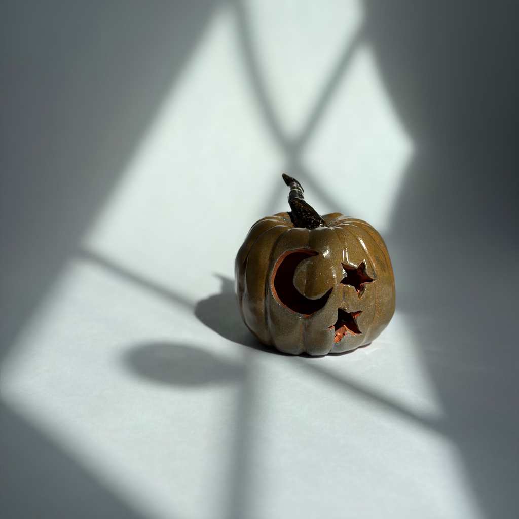 A small carved jack-o'-lantern pumpkin with a crescent moon and star cutout, placed on a white surface under dramatic window-shadow lighting.