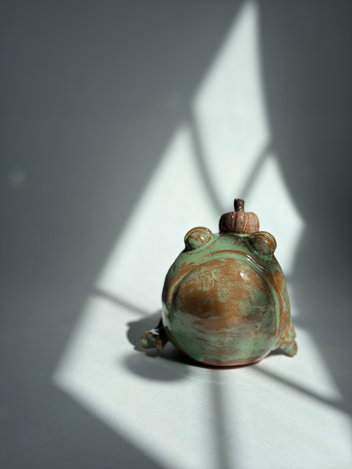 a green terracotta frog wearing a pumpkin hat