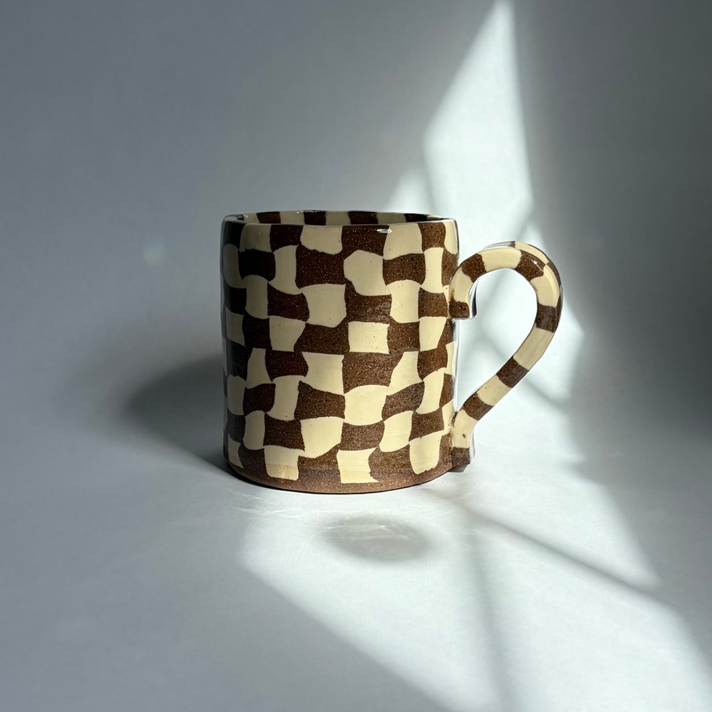 A brown and beige checkered ceramic mug against a white background.