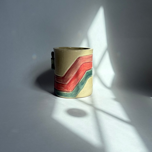A beige mug with teal, pink, and purple accents on a white background.