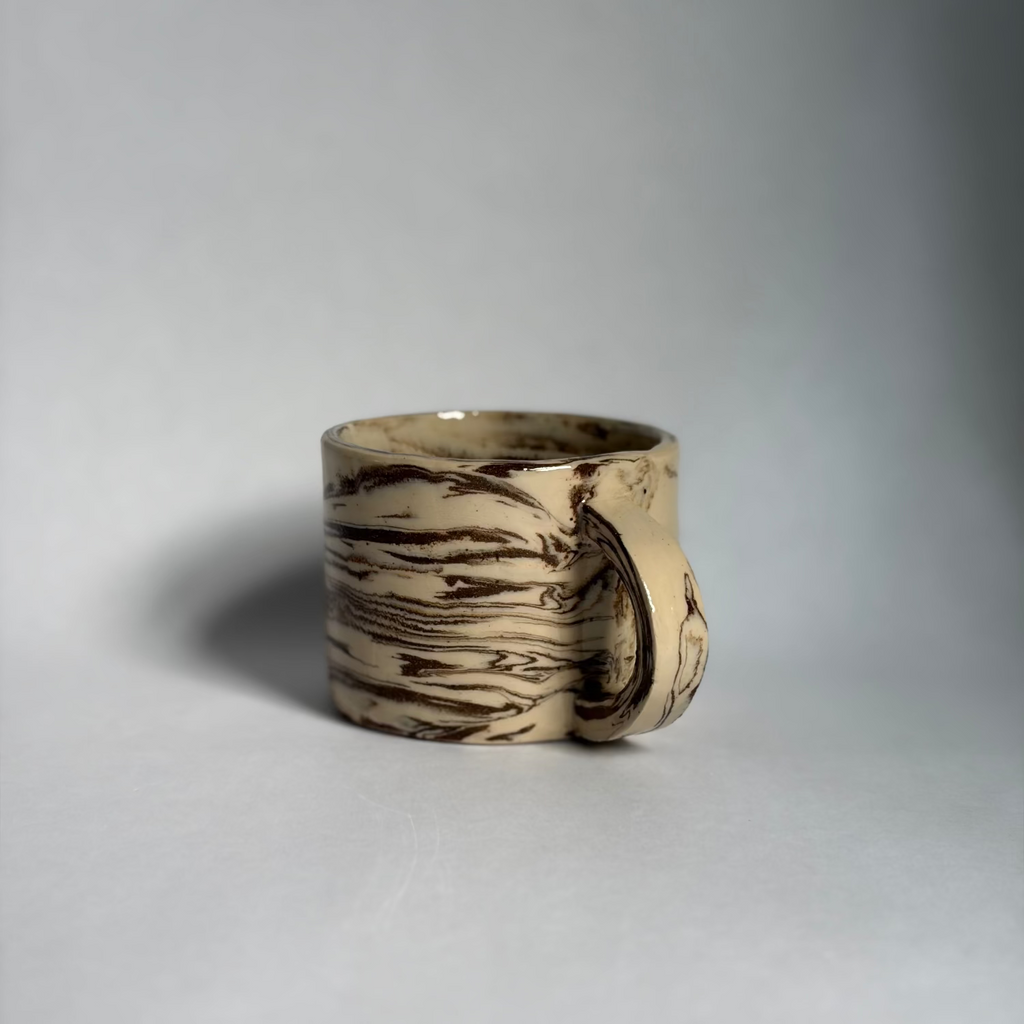 A ceramic mug with a textured, bark-like brown and beige pattern, photographed on a neutral gray background.