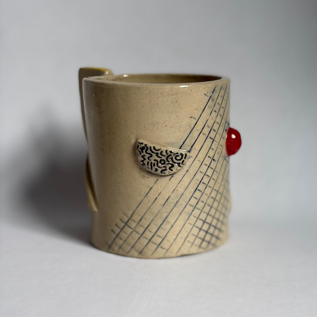 A handmade ceramic mug with a textured beige body, a yellow-gold glazed rim, and a small yellow geometric pattern on the side, set against a neutral gray background.