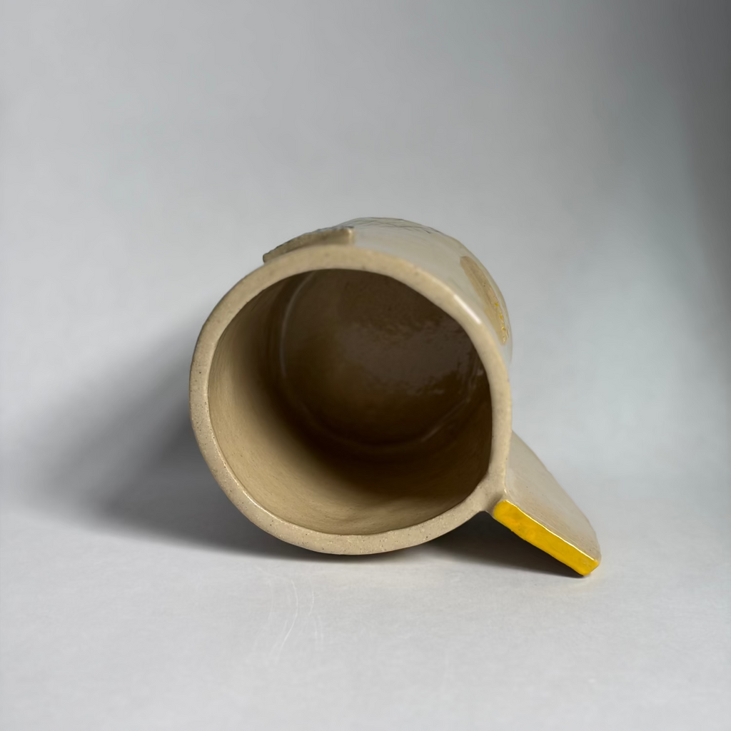 A handmade ceramic vessel shown on its side. The exterior is glazed in a warm beige/cream color.