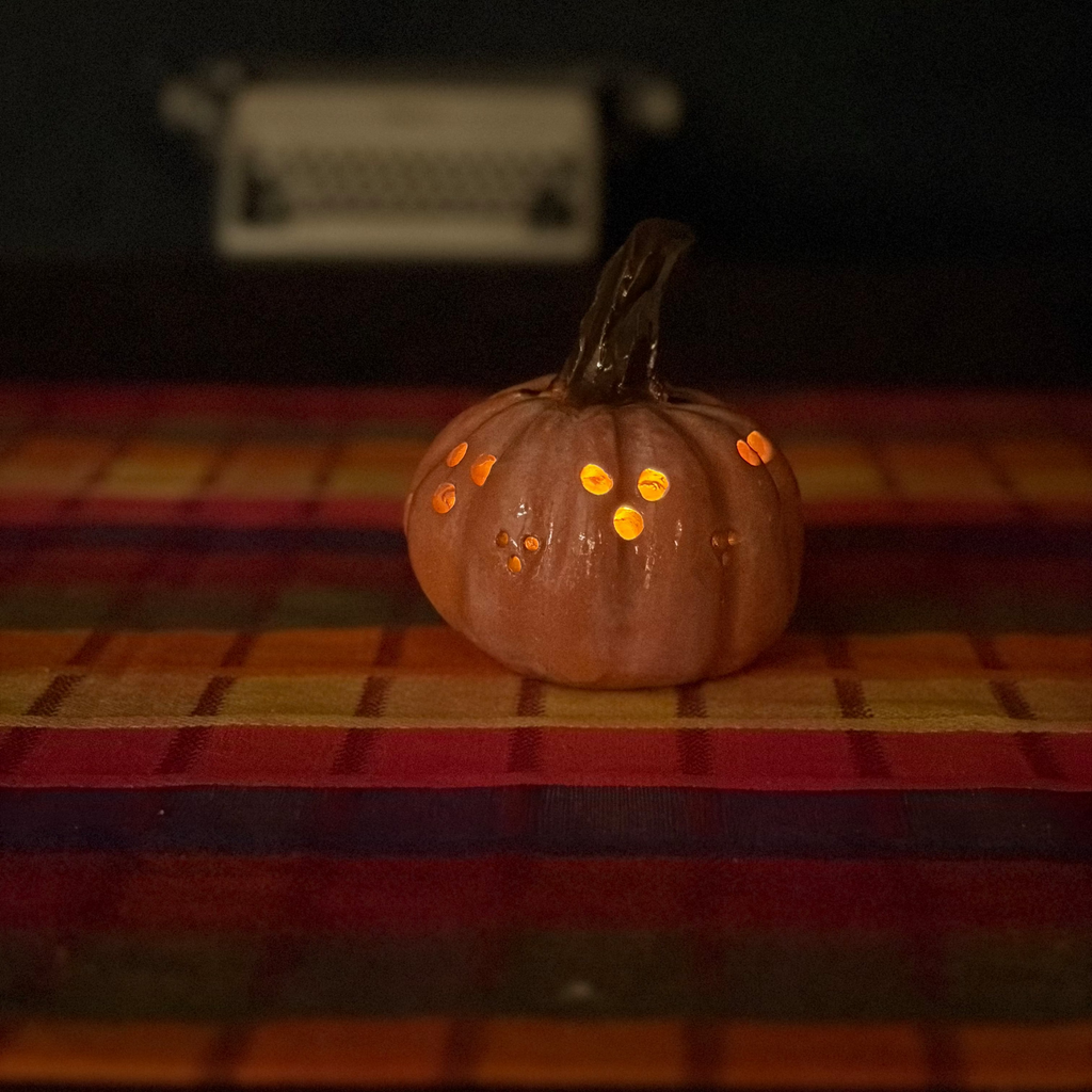 A carved jack-o'-lantern pumpkin with a lit orange glow inside, placed on a striped red, orange, and yellow blanket against a dark background.
