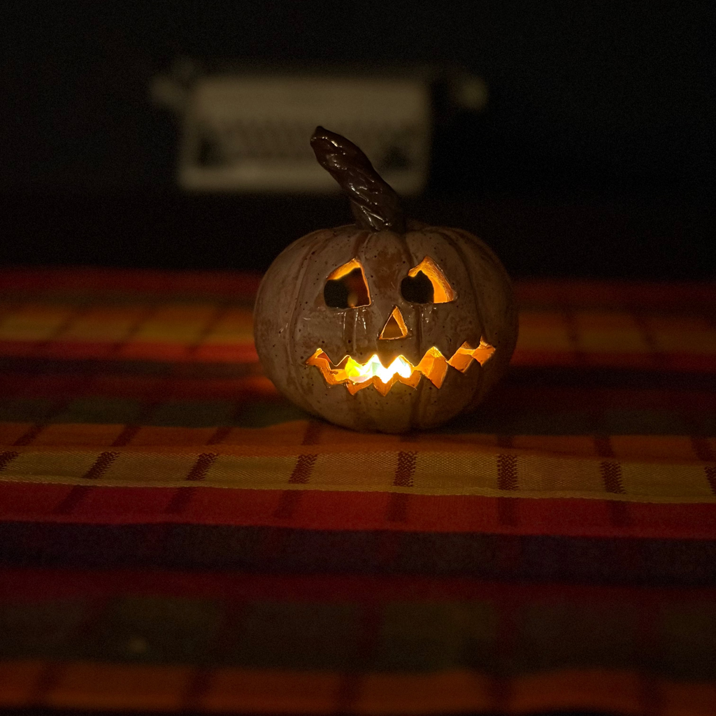 A carved jack-o'-lantern pumpkin with a lit orange glow inside, placed on a striped red, orange, and yellow blanket against a dark background.
