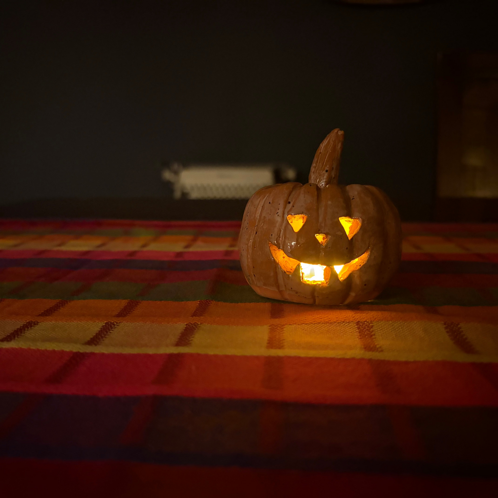 A carved jack-o'-lantern pumpkin with a lit orange glow inside, placed on a striped red, orange, and yellow blanket against a dark background.
