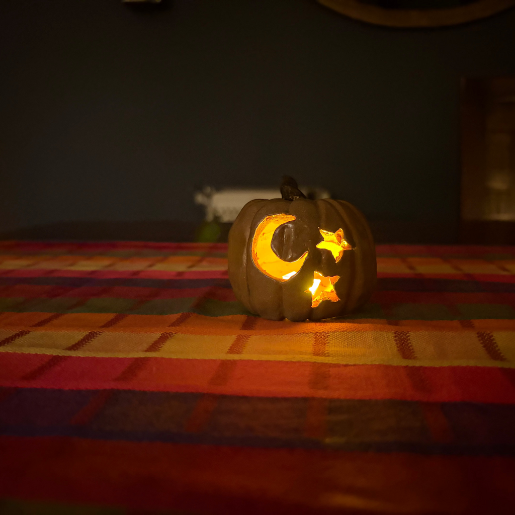 A carved jack-o'-lantern pumpkin with a glowing yellow crescent moon and star face, sitting on a colorful striped blanket in a dimly lit room.