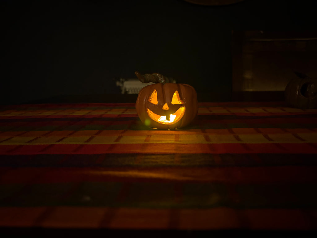 A carved jack-o'-lantern pumpkin glowing with warm orange light on a dark table with a red and yellow plaid surface.