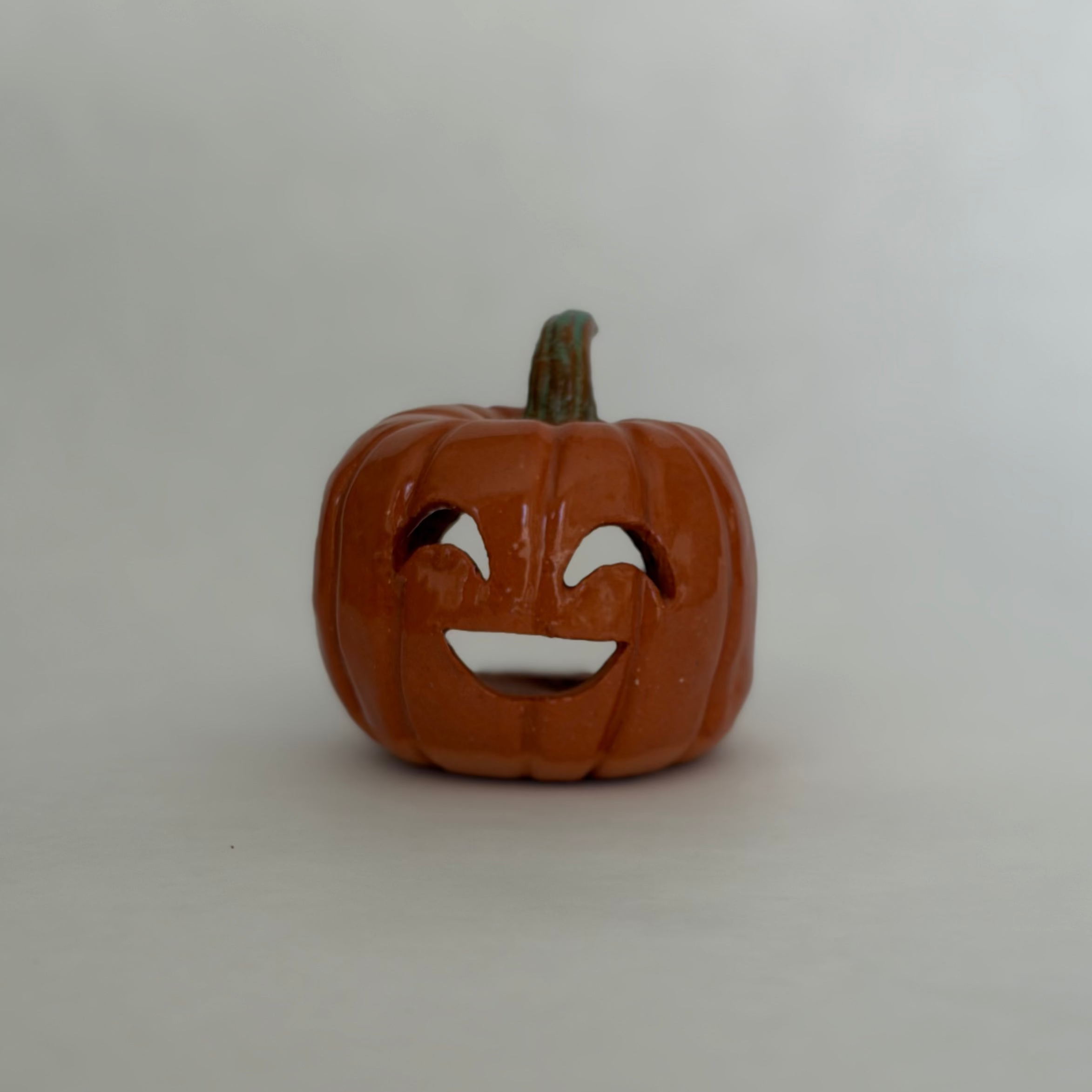 A small carved orange jack-o'-lantern pumpkin figurine with a green stem, photographed on a white surface