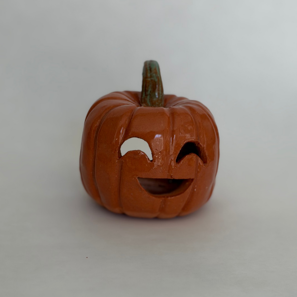 A small carved orange jack-o'-lantern pumpkin figurine with a green stem, photographed on a white surface