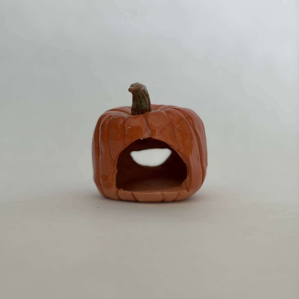 Back view of a small carved orange jack-o'-lantern pumpkin figurine with a green stem, showing a space for a tealight.
