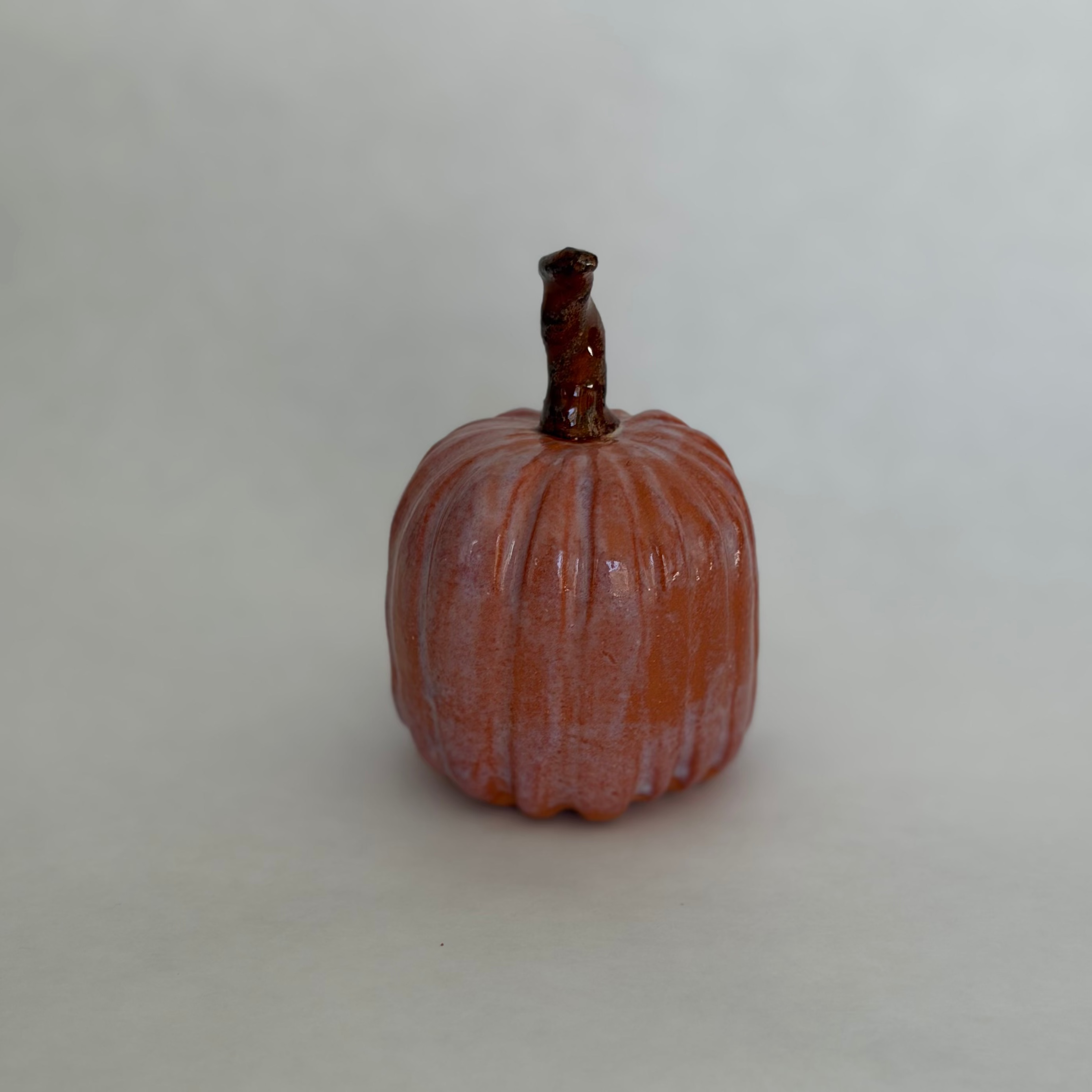 Single terracotta-blush ceramic pumpkin with a tall dark stem, photographed on a plain white background
