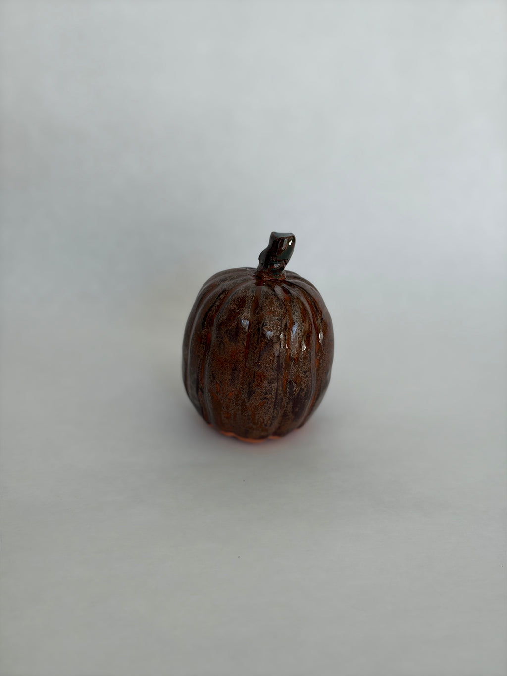 Single tall dark brown ceramic pumpkin with a small dark stem, glossy textured glaze, photographed on a white background
