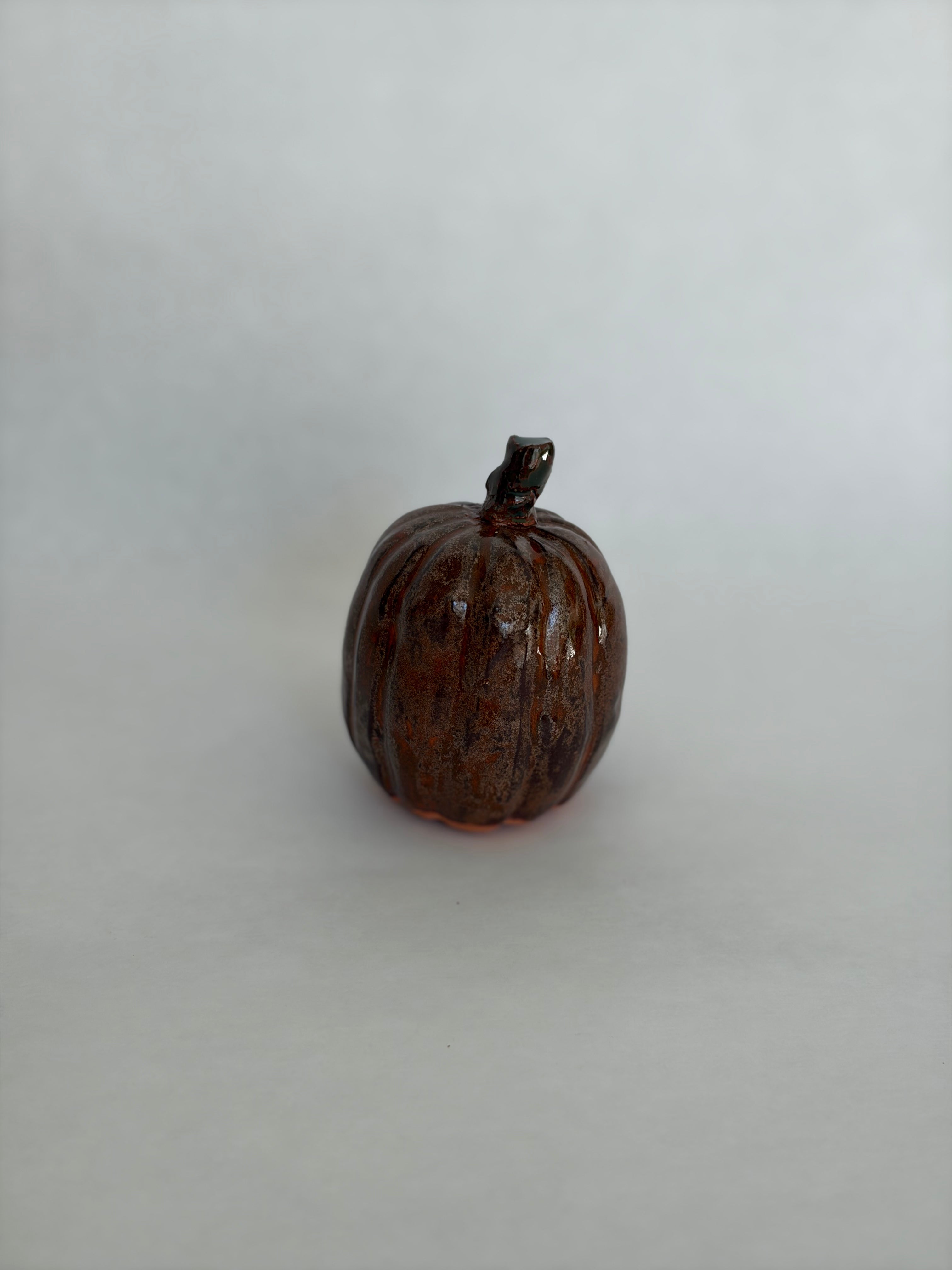 Single tall dark brown ceramic pumpkin with a small dark stem, glossy textured glaze, photographed on a white background
